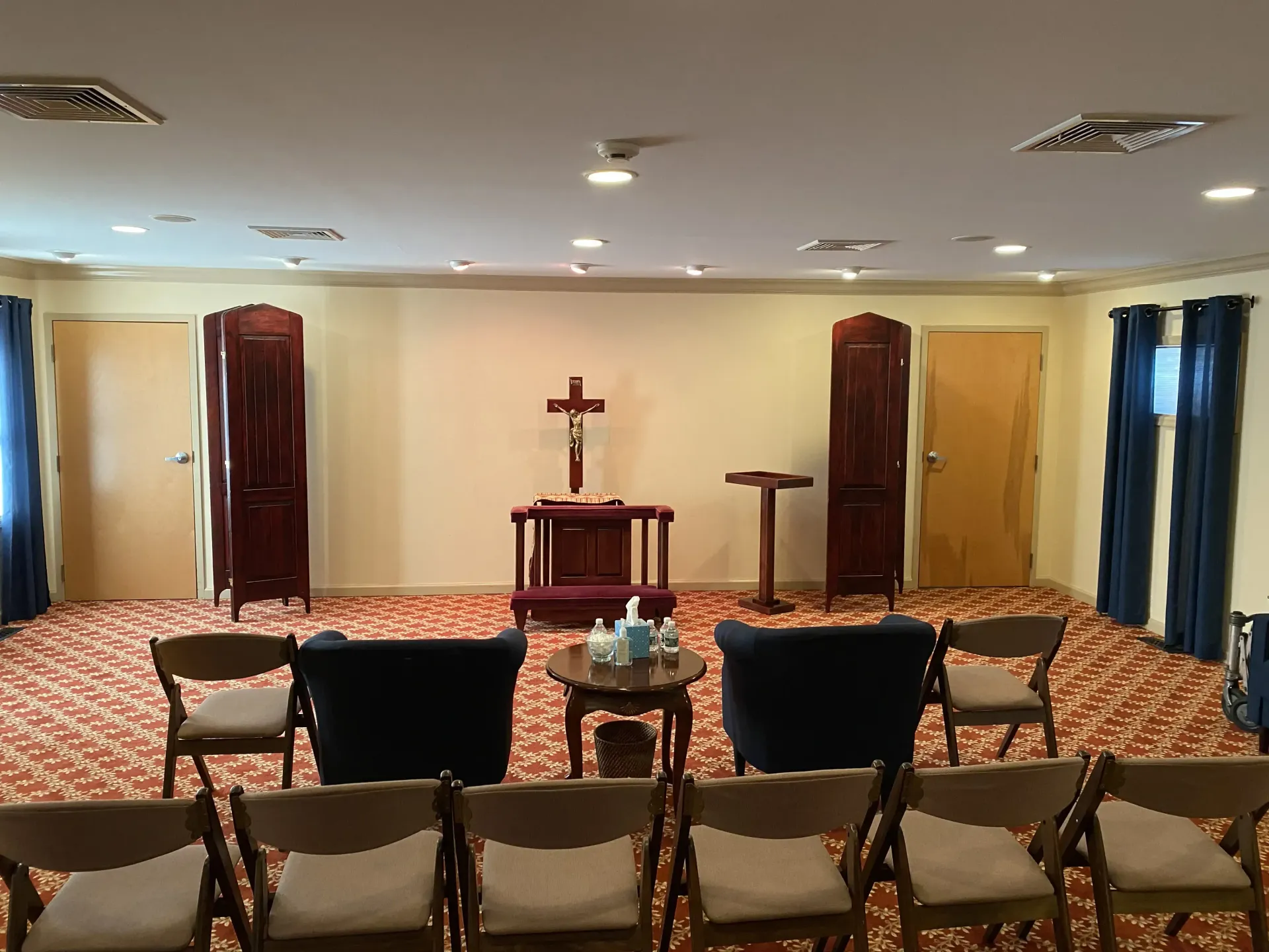A funeral home chapel. A cross on a stand is centered. Chairs are arranged for a service.