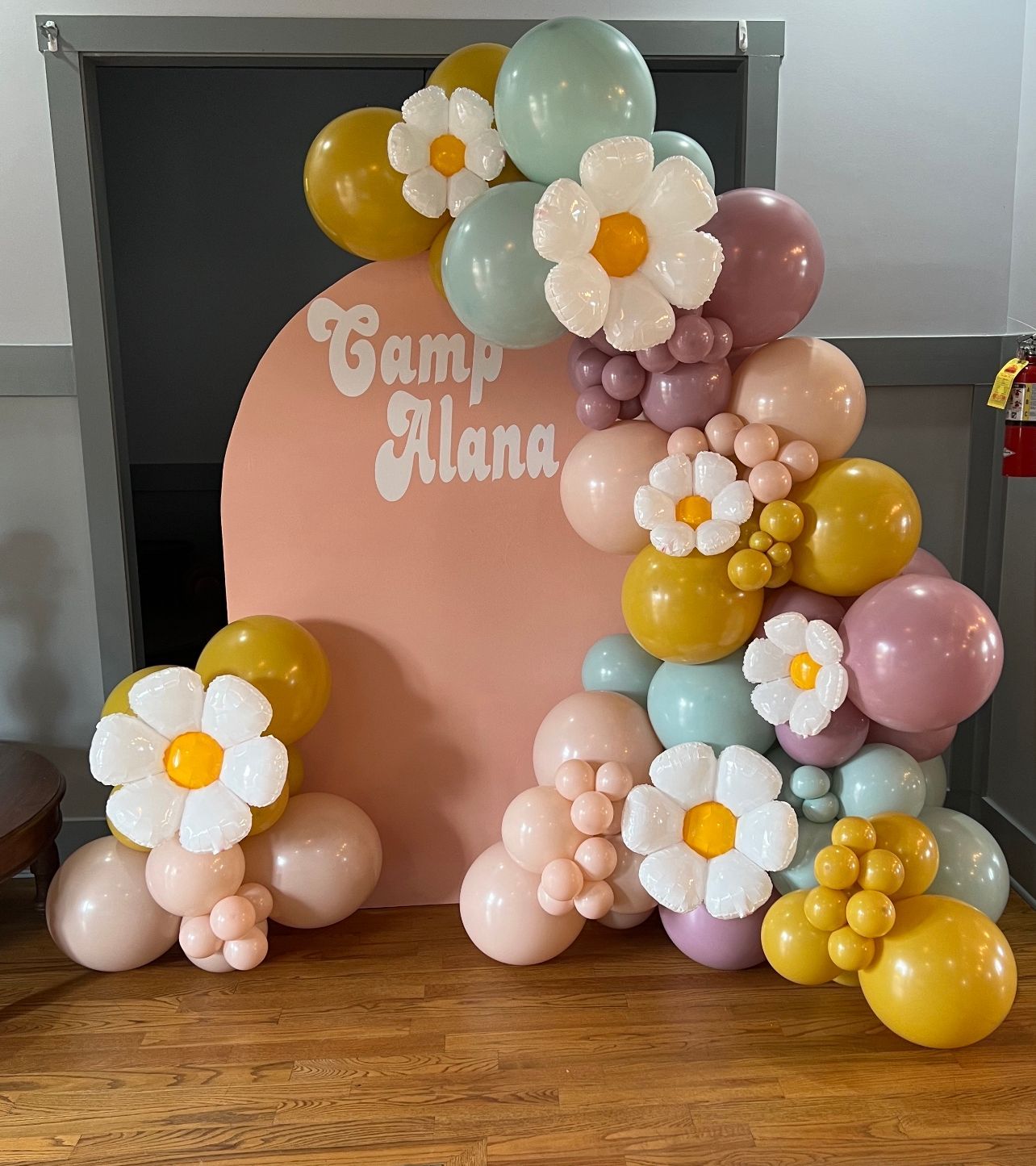 A party setup with a pink arch, balloons in various pastel colors, and daisy decorations.