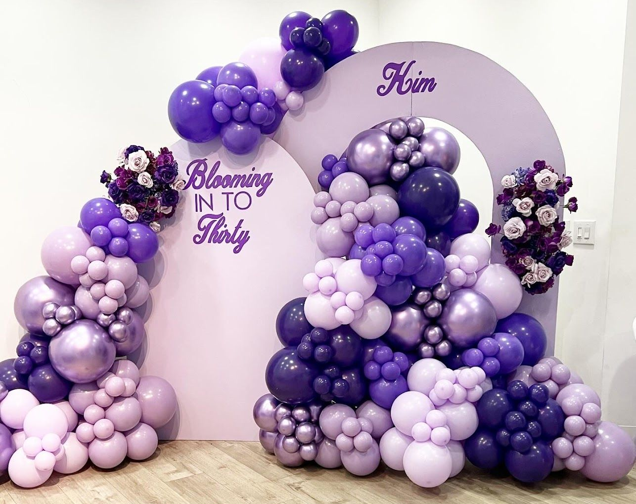 Purple balloon arch with floral accents for a 