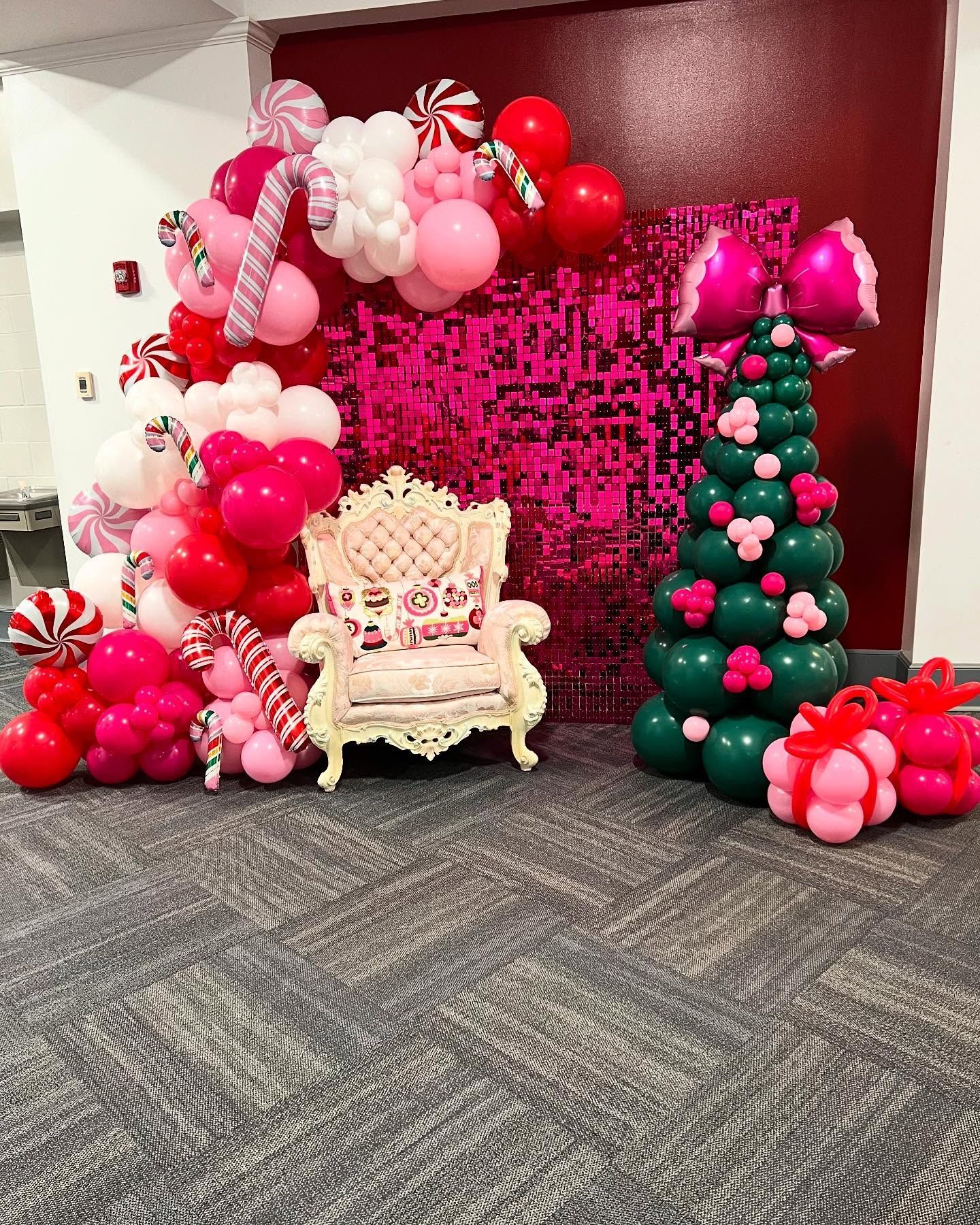 Christmas-themed decor: pink and red balloon arch, chair, sequin backdrop, balloon tree, and gifts.