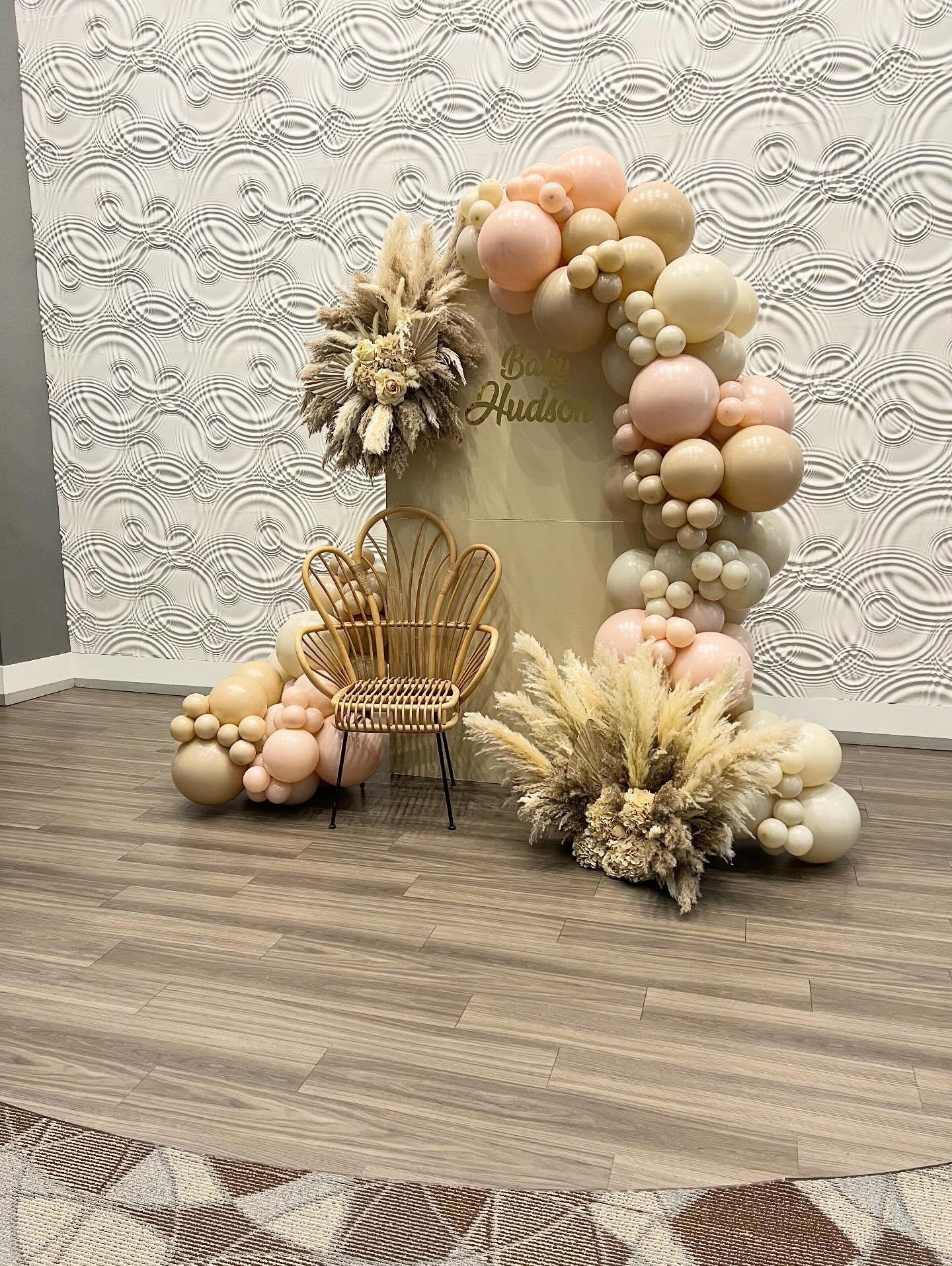 Balloon arch with pampas grass and a miniature chair, against a patterned wall.