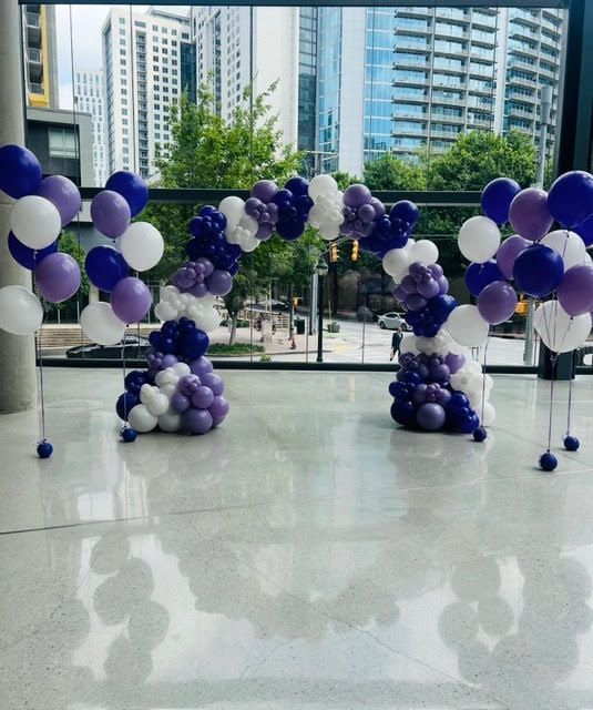 Purple and white balloon archway with supporting clusters, indoors with city view.