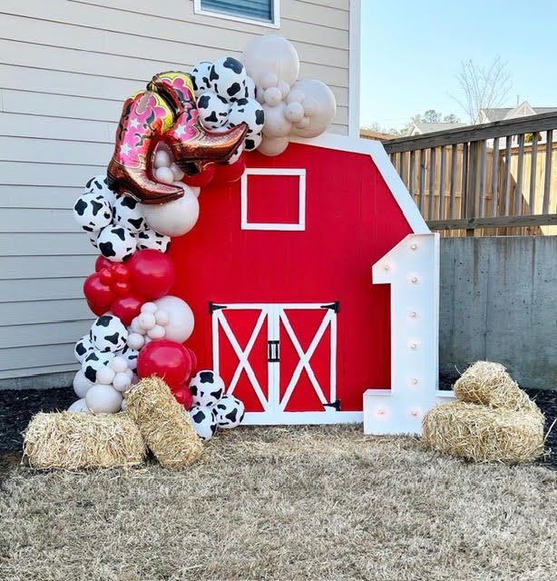 Barn-themed first birthday backdrop. Red barn cutout with the number one, balloon arch, hay bales.