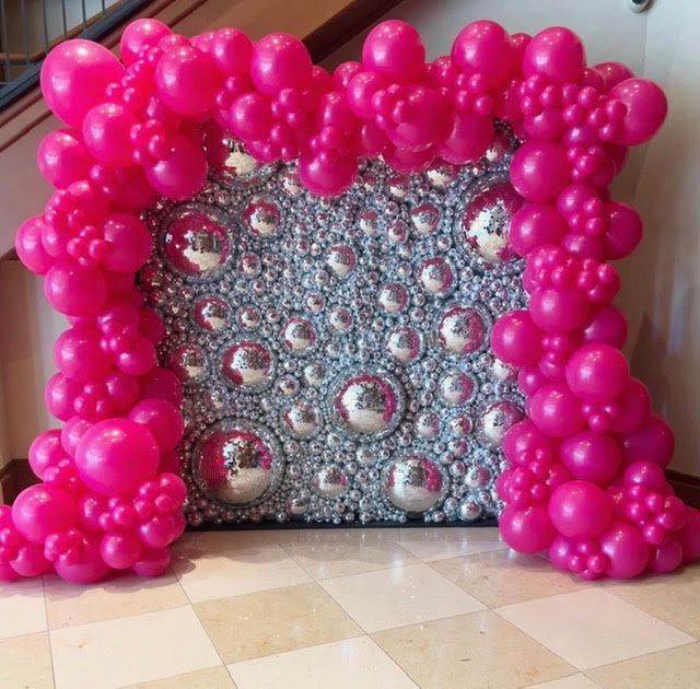Pink balloon arch framing a silver mirrored backdrop.