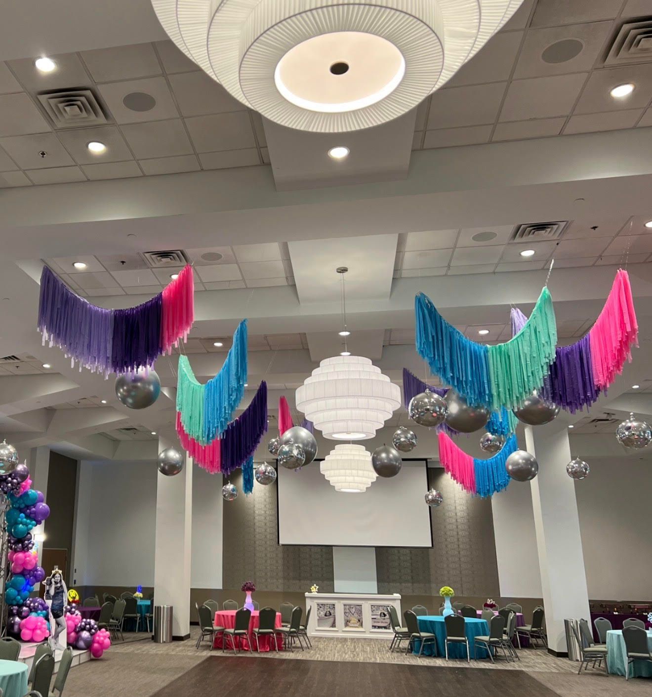 Festive event hall decorated with hanging fringe, disco balls, and colorful balloons.