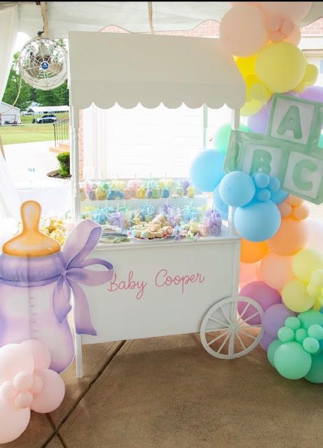 Baby shower cart with candy and balloon decorations, pastel colors, and a baby bottle prop.