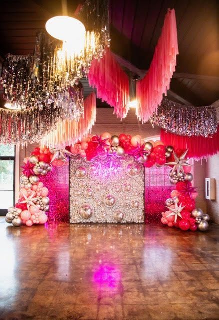 Event backdrop with balloons, tinsel, and pink decor.