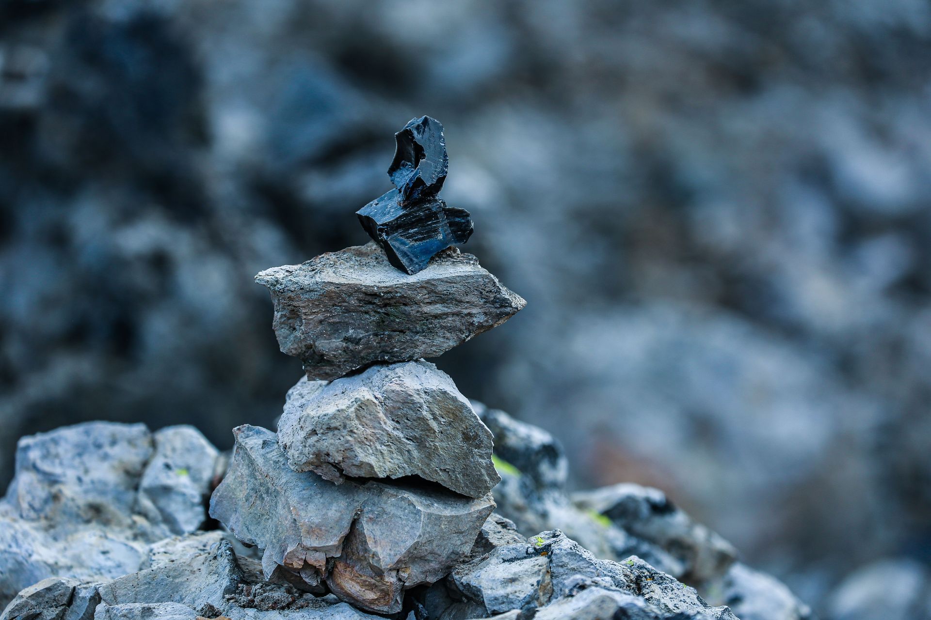 Stacked stones with a small dark figurine on top against a blurred rocky background