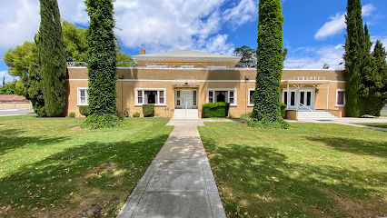 Brick building with white trim and tall trees, seen from a sidewalk across a green lawn