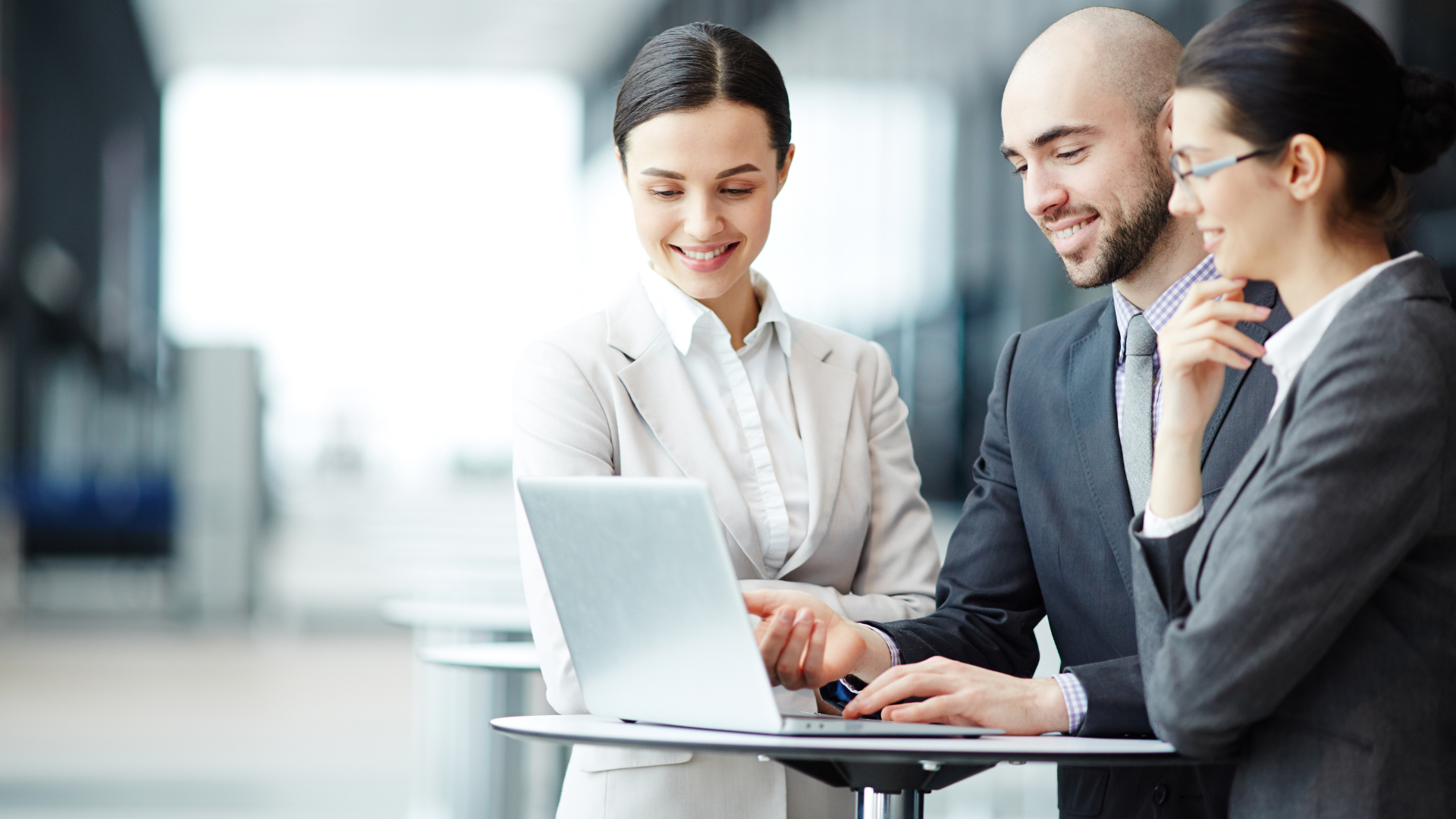 Picture of three people working at a laptop computer screen, pointing and smiling