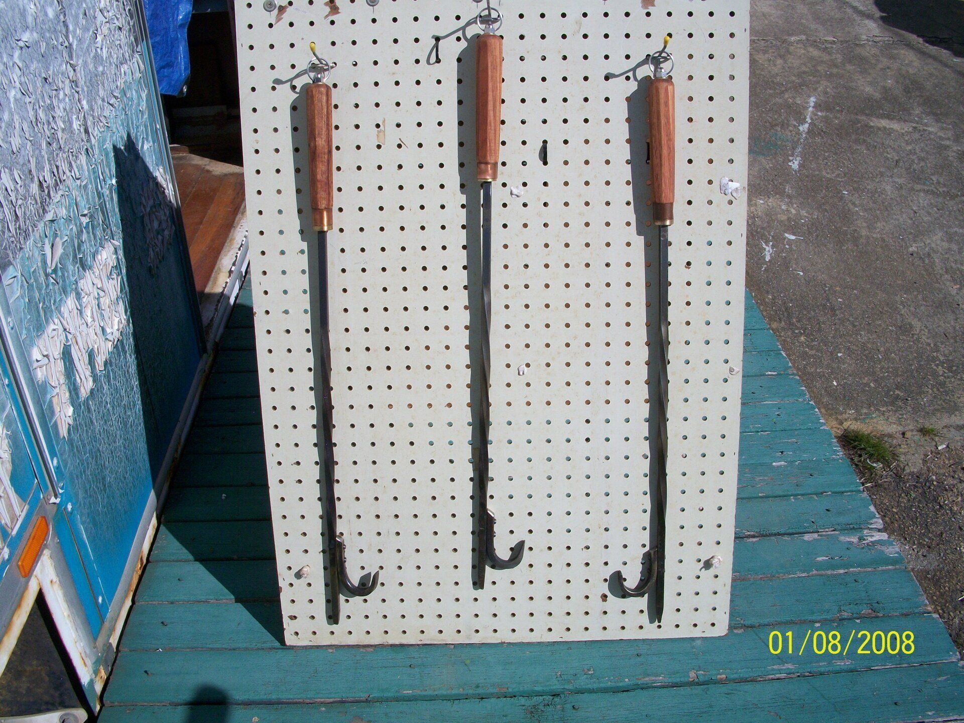 Three black crowbars with wooden handles hanging on a pegboard outdoors