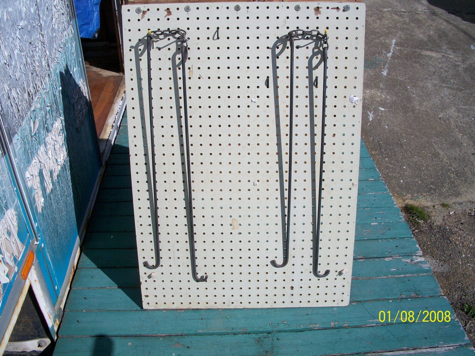 Two black metal hooks mounted on a white pegboard, photographed outdoors on a teal table.