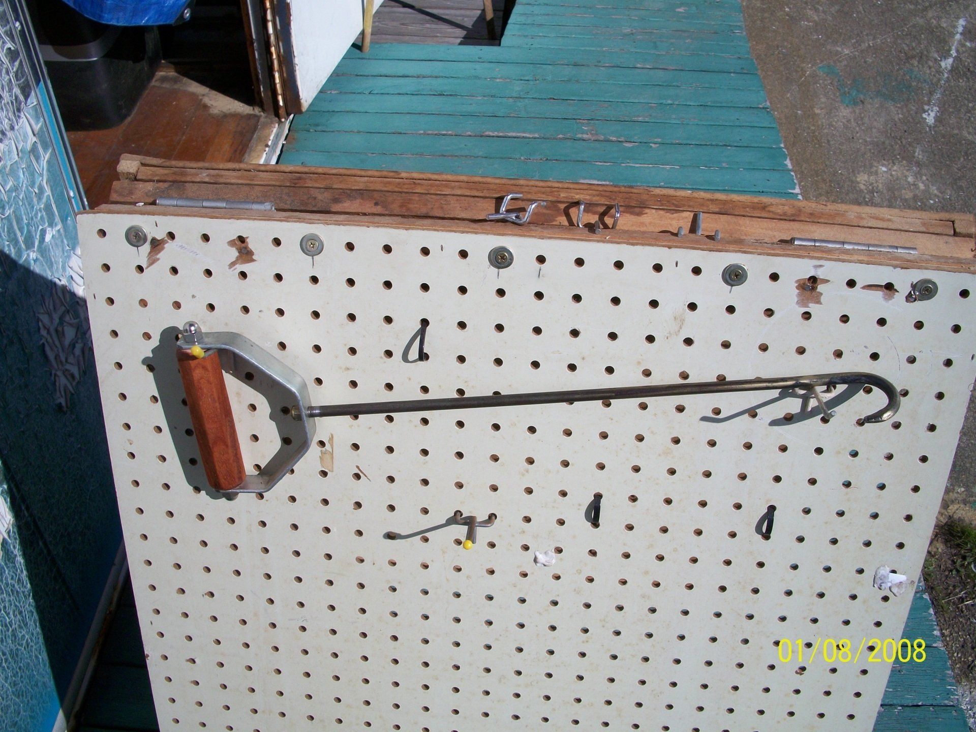 Close-up of a white pegboard with a long black metal tool and orange handle, indoors on a table