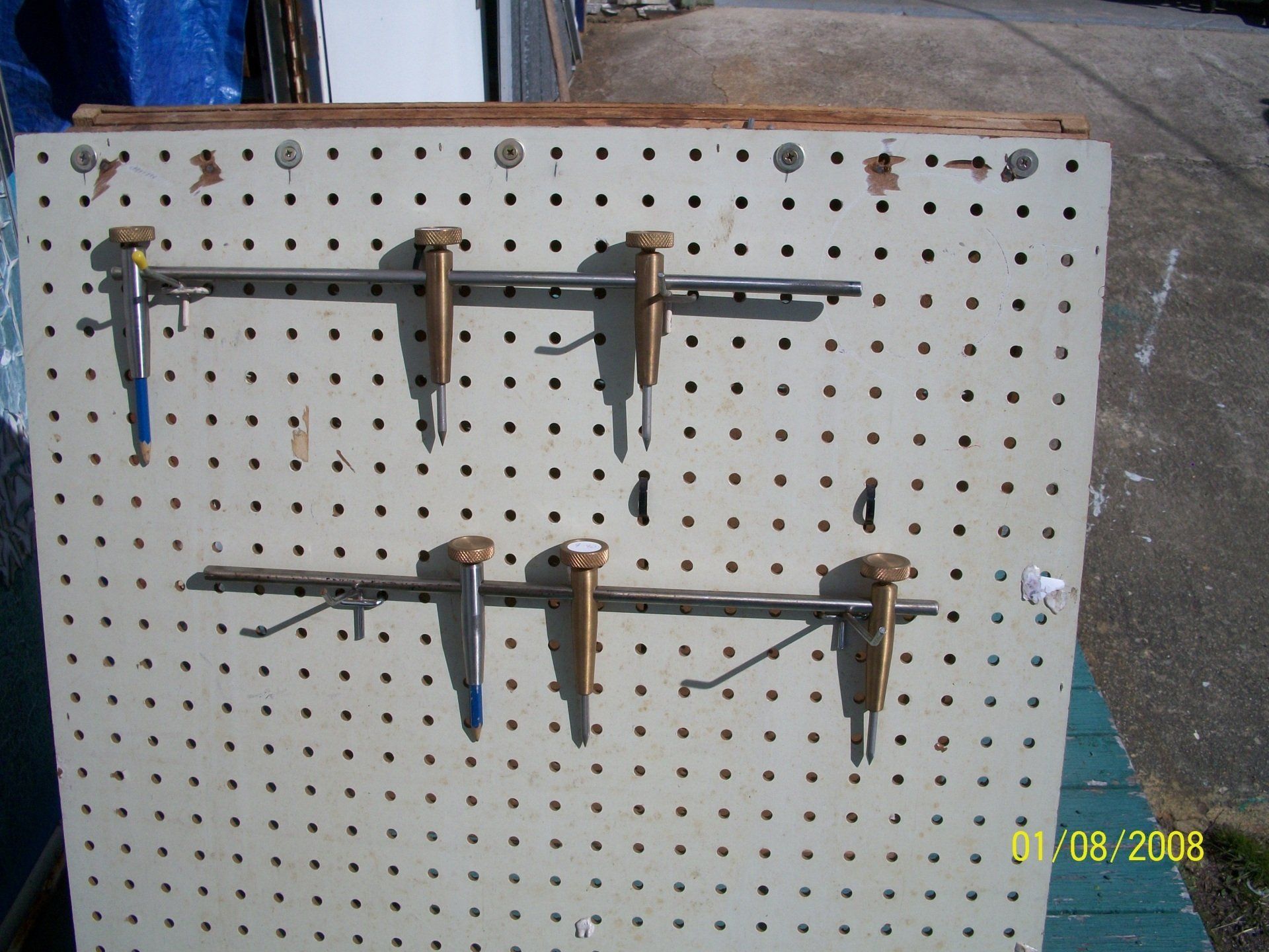 Pegboard wall with two horizontal metal bars and several clamps, in a workshop setting