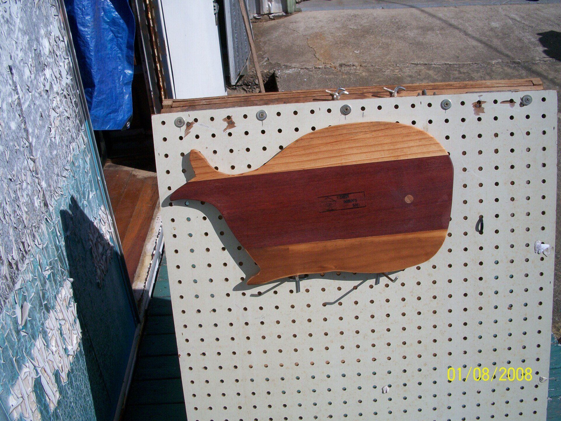 Wooden fish-shaped sign mounted on a pegboard, with a dark red body and light tan head.