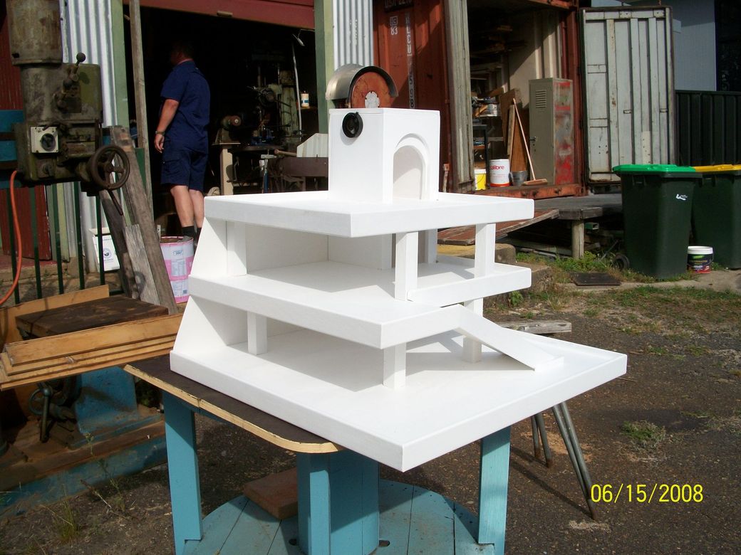 White multi-tiered model on a table in a workshop area, with a person standing in the background.