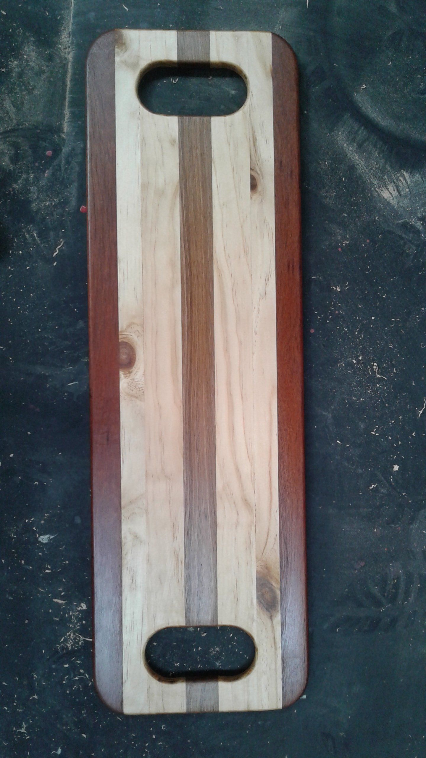 Wooden cutting board with oval handle cutouts, dark brown sides, and light center stripe.