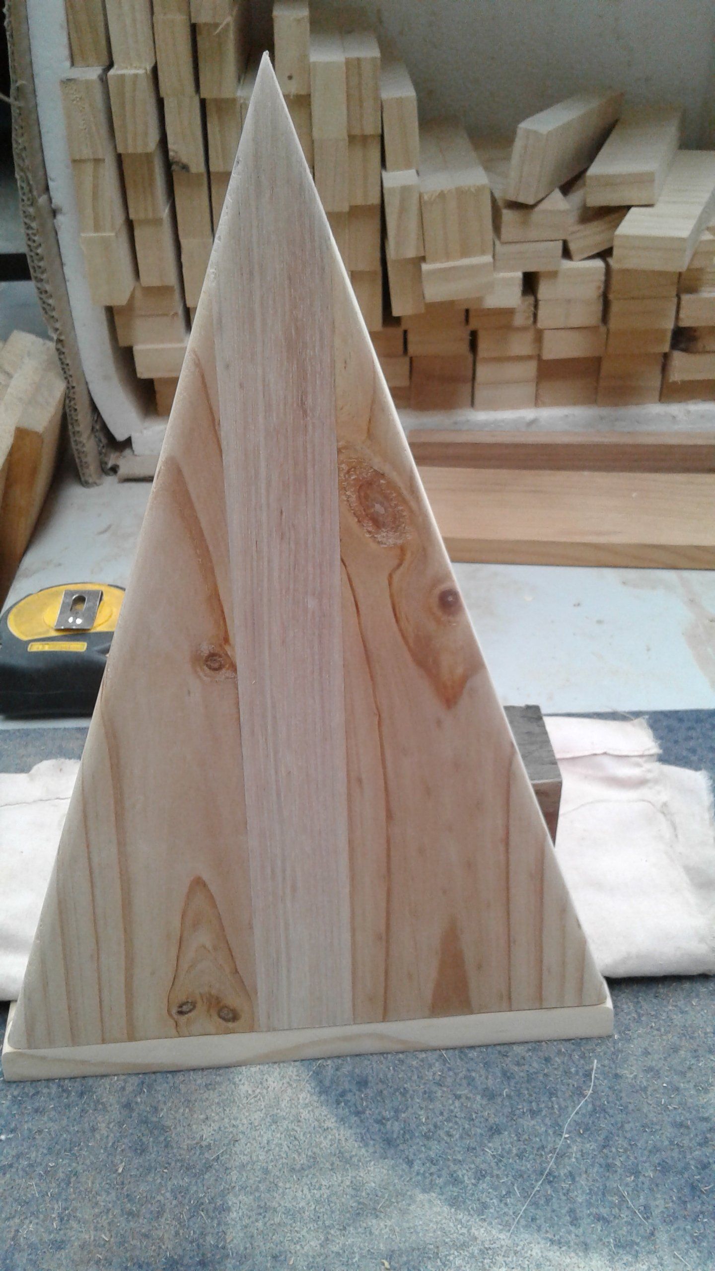 Wooden triangular pyramid on a workshop floor with stacked lumber in the background