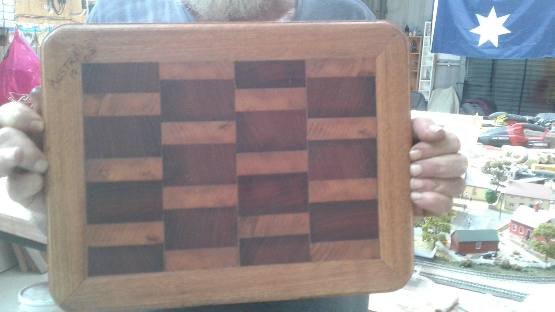 A wooden checkered board with a thick frame, held up by two hands indoors.