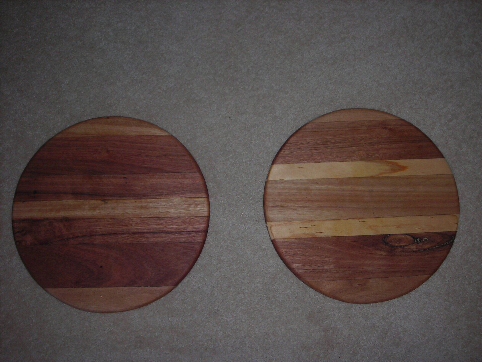 Two round wooden cutting boards on a gray carpet, one dark wood and one striped light and dark wood