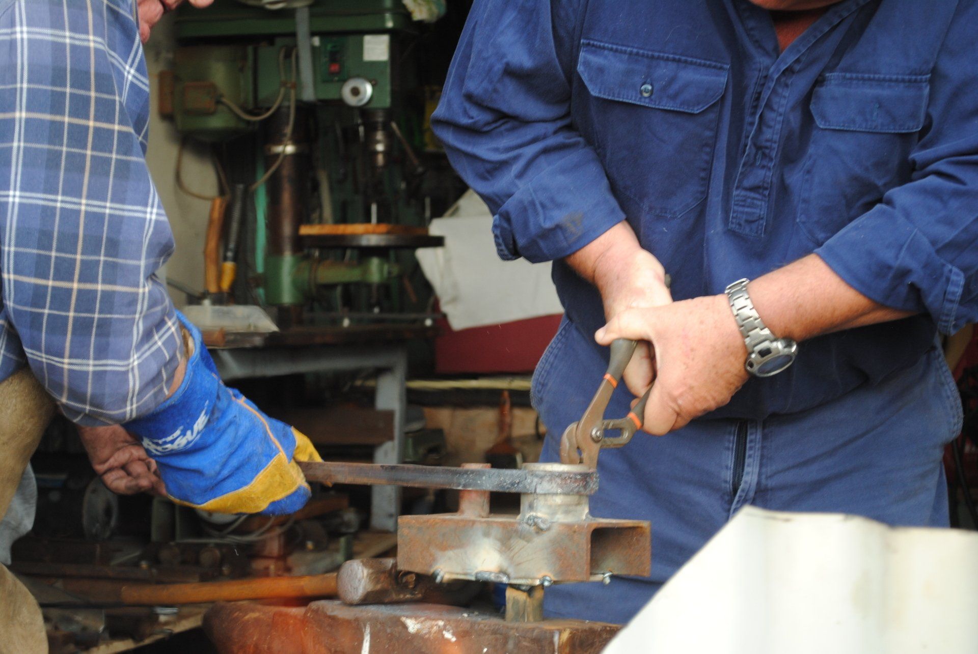 Two workers in blue shirts operating industrial machinery with metal tools and sparks