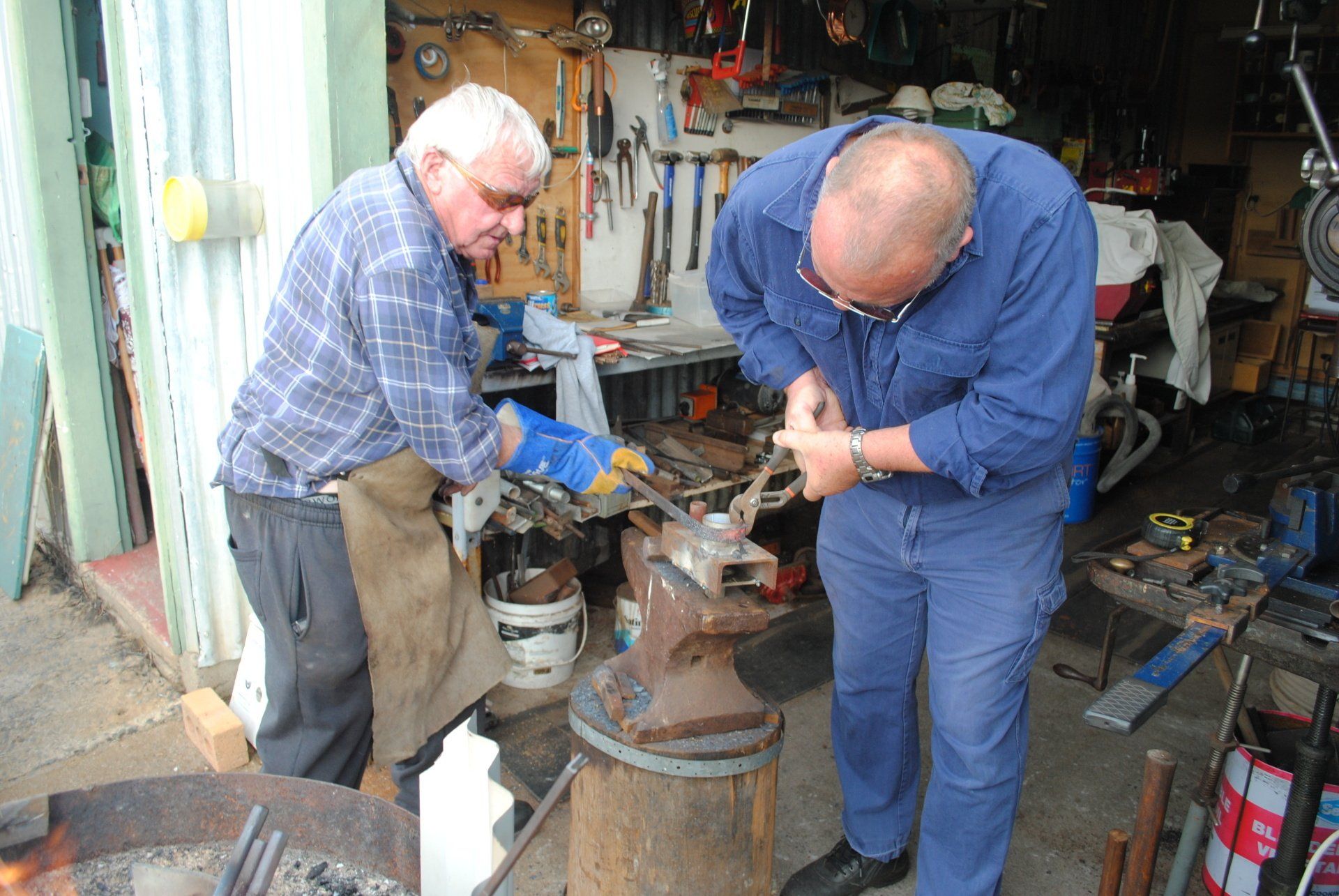Two men in a workshop using tools to repair a metal part on a workbench
