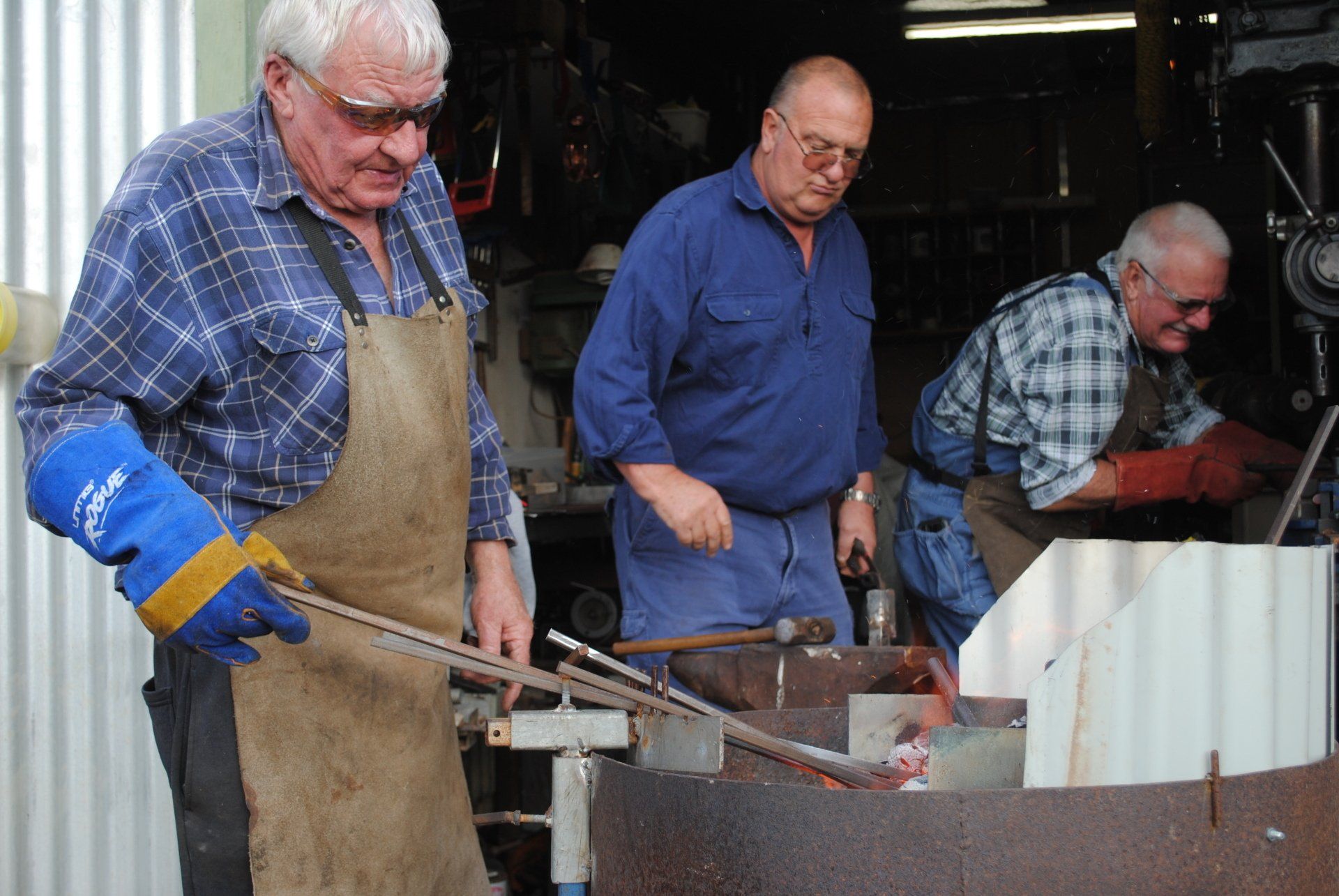 Three men working in a metal shop, stirring molten metal in a large furnace.