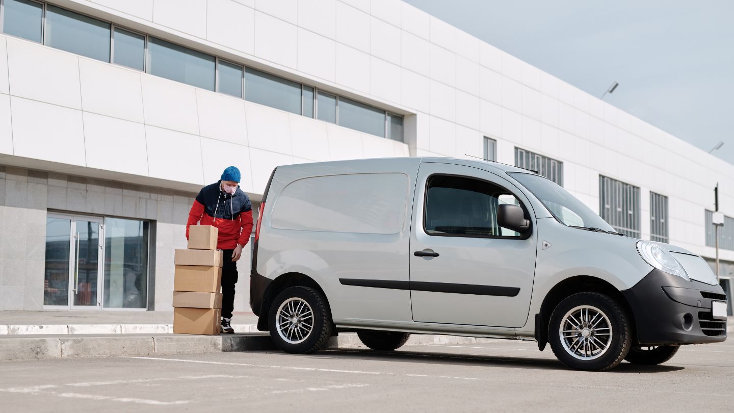 Delivery worker unloading boxes beside a white van outside a modern building