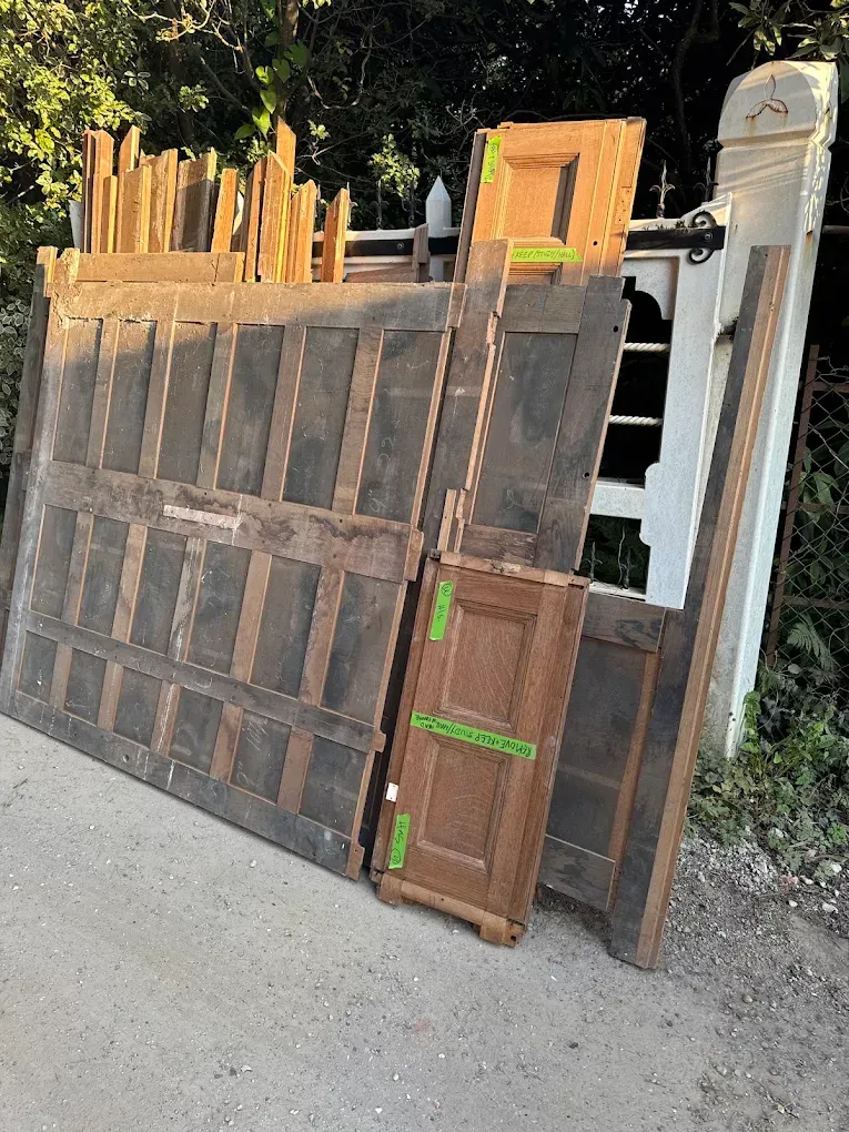 Large wooden paneling, door fragments, and molding leaning on a white structure outdoors on a gravel surface.