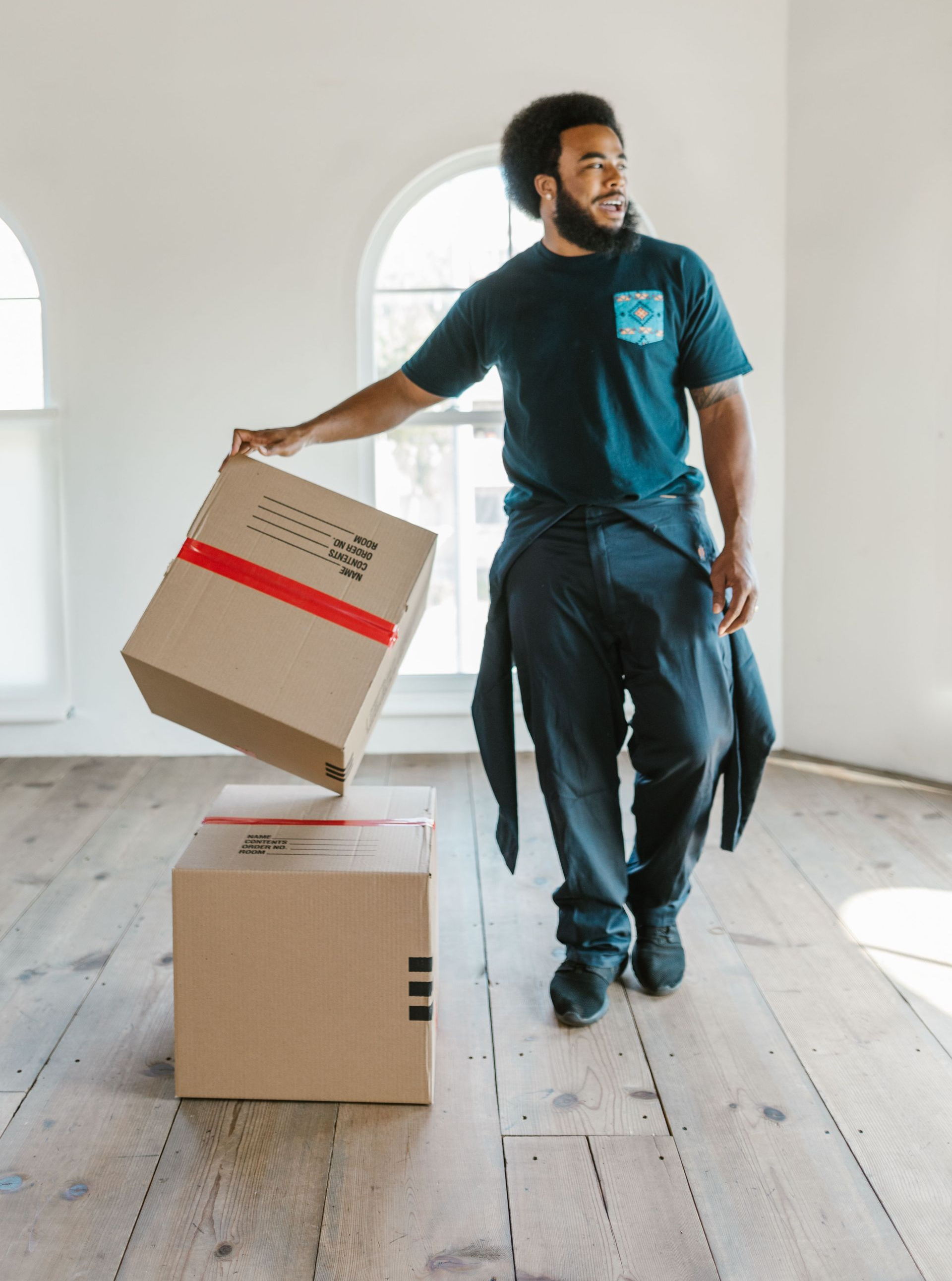 Man moving cardboard boxes in a bright, empty room with wooden floors
