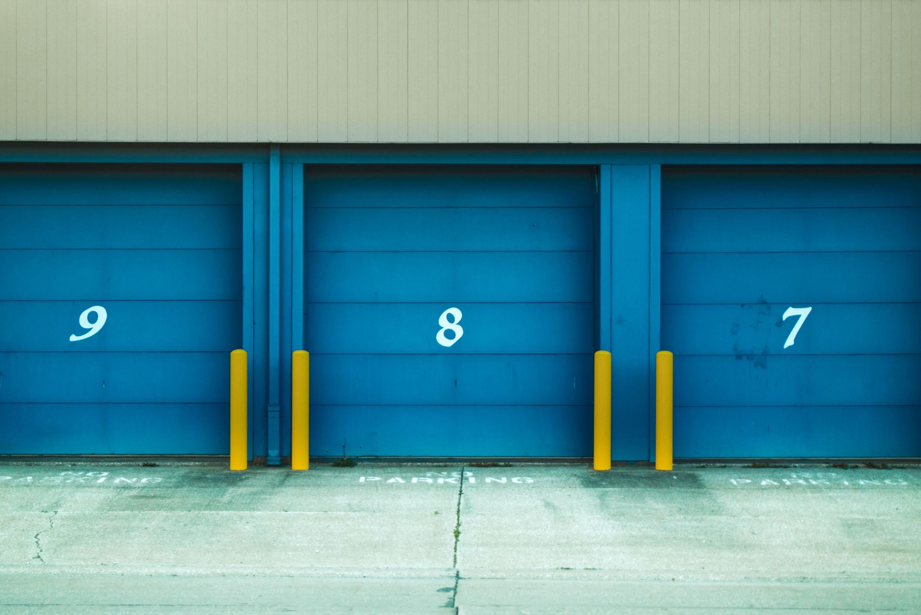Three blue garage doors numbered 9, 8, and 7 with yellow posts in front