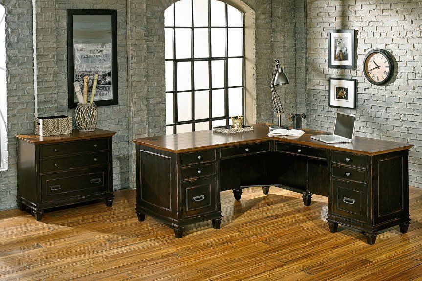 An L-shaped desk and storage unit in a rustic office with brick walls and large window.