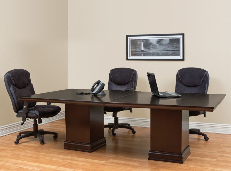 Conference room with dark wood table, three office chairs, laptop, phone. Painting on beige wall.