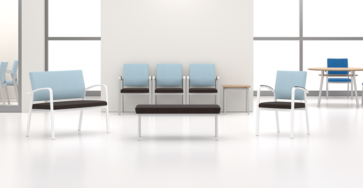 Waiting room with light blue chairs and a dark bench against a white wall and large windows.