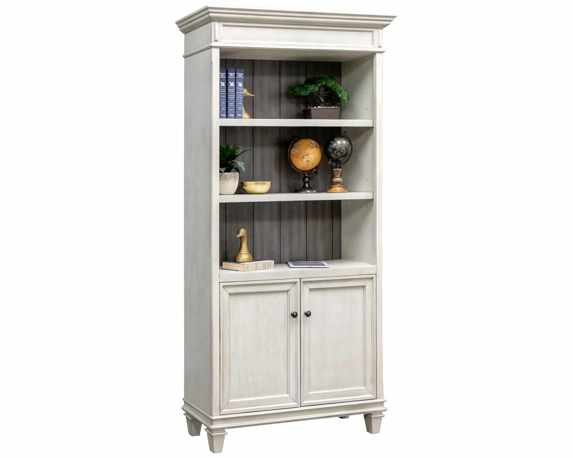 White wooden bookshelf with two cabinet doors and three shelves displaying books and decorative items.