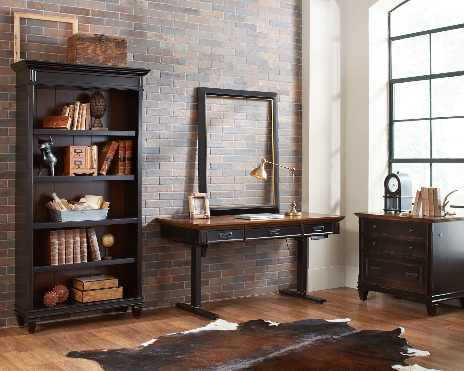 Home office with a black desk, bookshelf, and brick wall. Cowhide rug on wood floor.