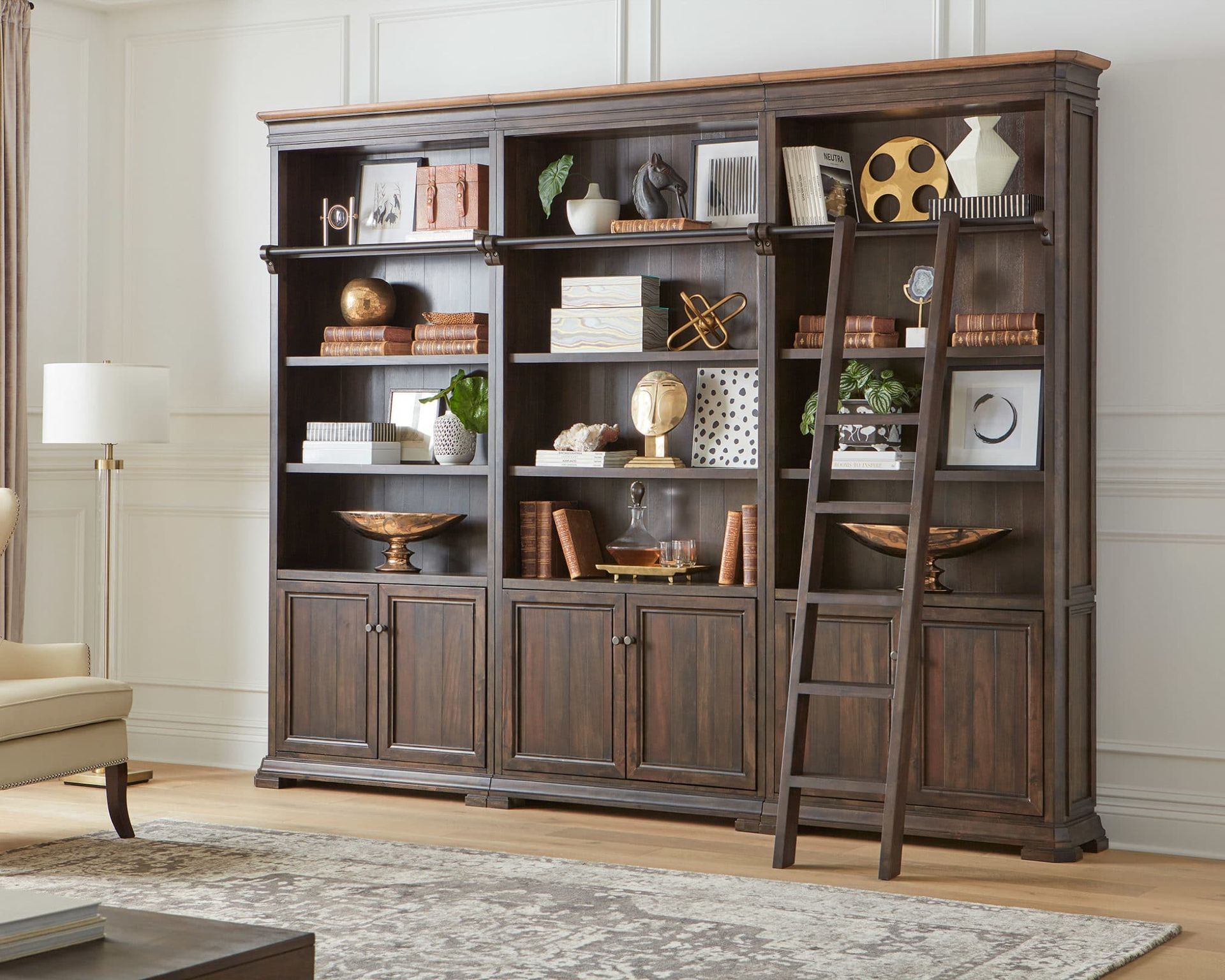 Large wooden bookcase filled with decor and a rolling ladder in a room.