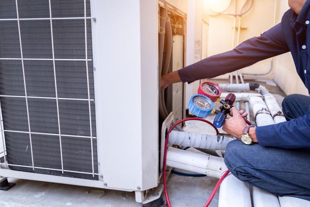 Technician using gauges to service an outdoor HVAC unit with hoses attached