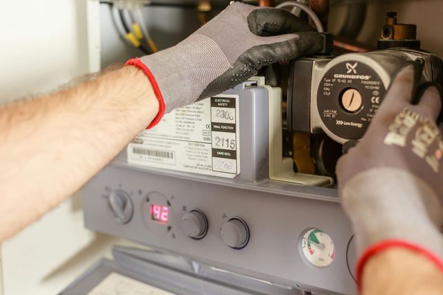 Gloved hands repairing a furnace control panel with gauges and wiring.