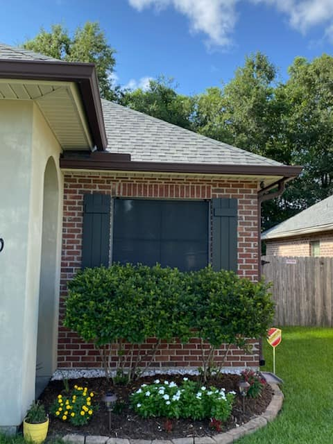 Brick home exterior with dark shutters, brown gutters, and a small garden.