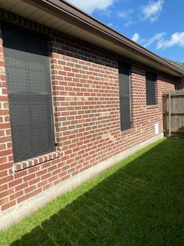 Brick exterior of a house with three windows, featuring dark screens, set against a blue sky.