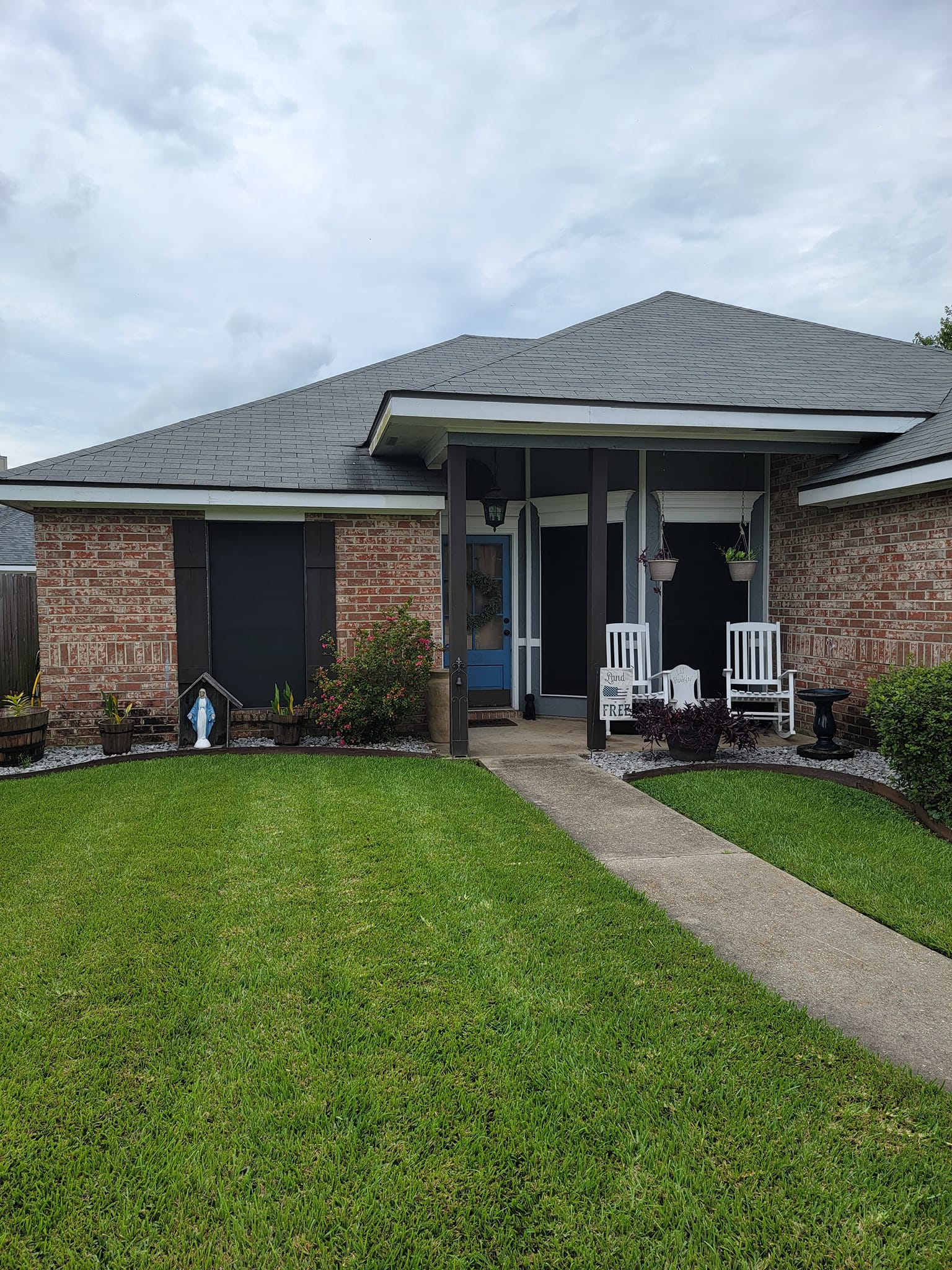 Brick house with gray roof and porch. Green lawn and walkway leading to the front door.