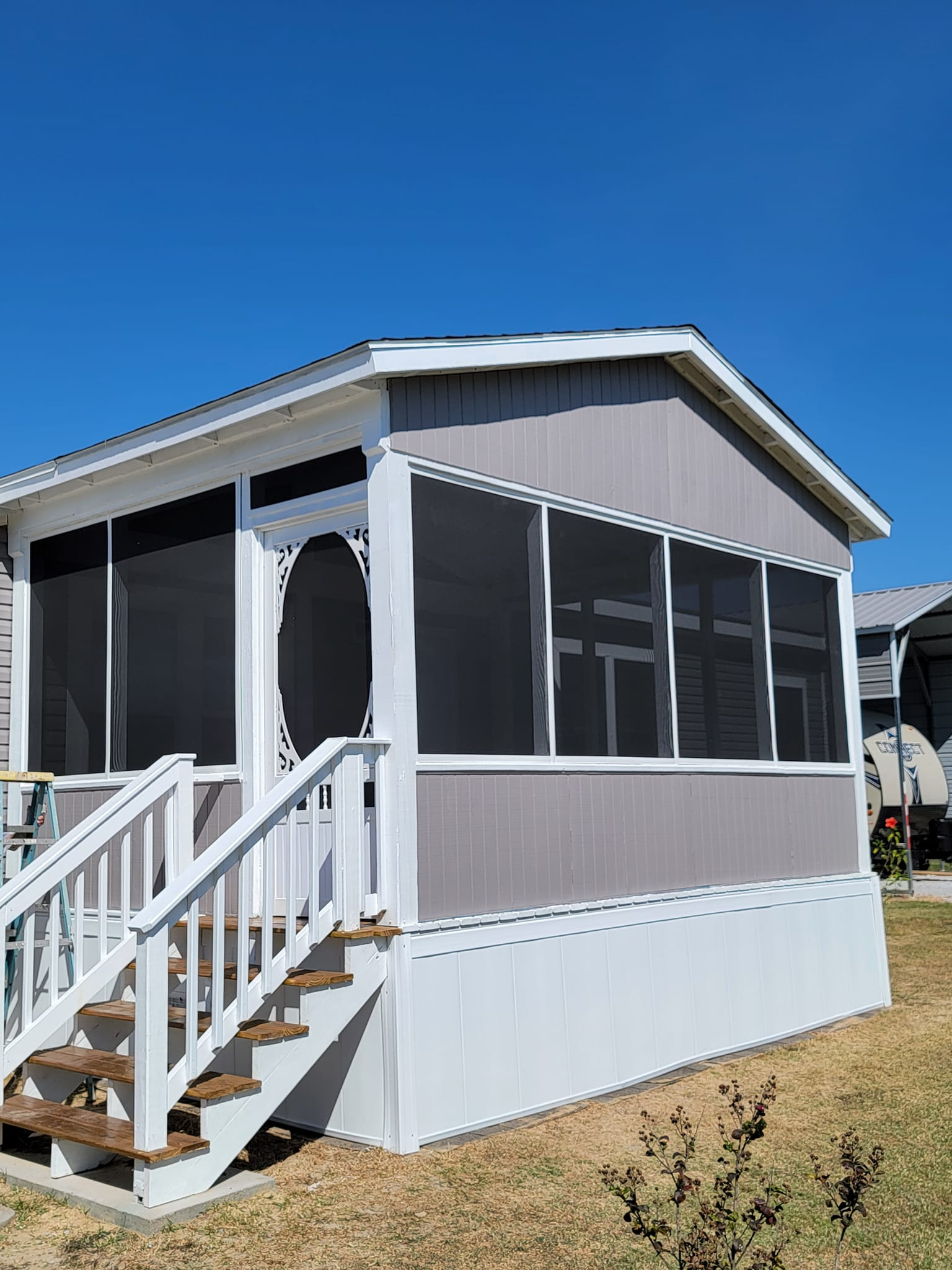 Screened porch with white stairs, light gray siding, and a blue sky background.