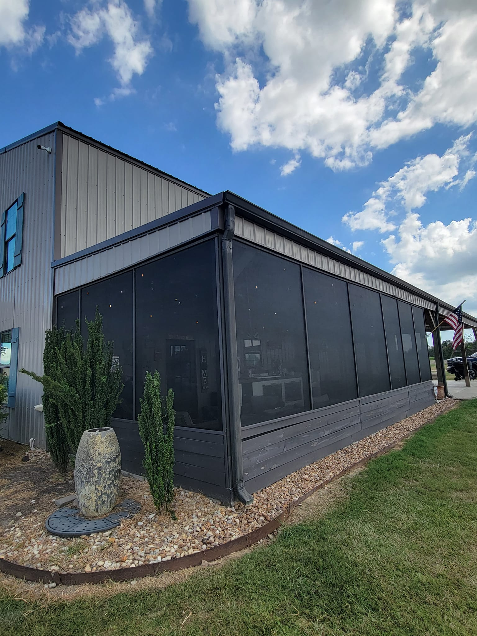 Building with a black screened-in patio, gravel landscaping, and a blue sky with clouds.
