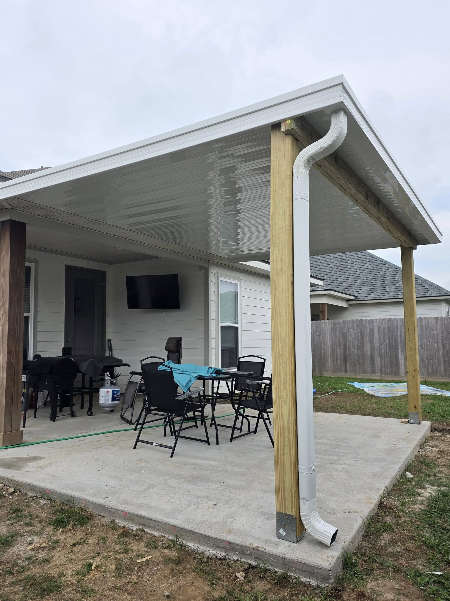 Concrete patio with covered seating area, table, chairs, TV, and gutter downspout.