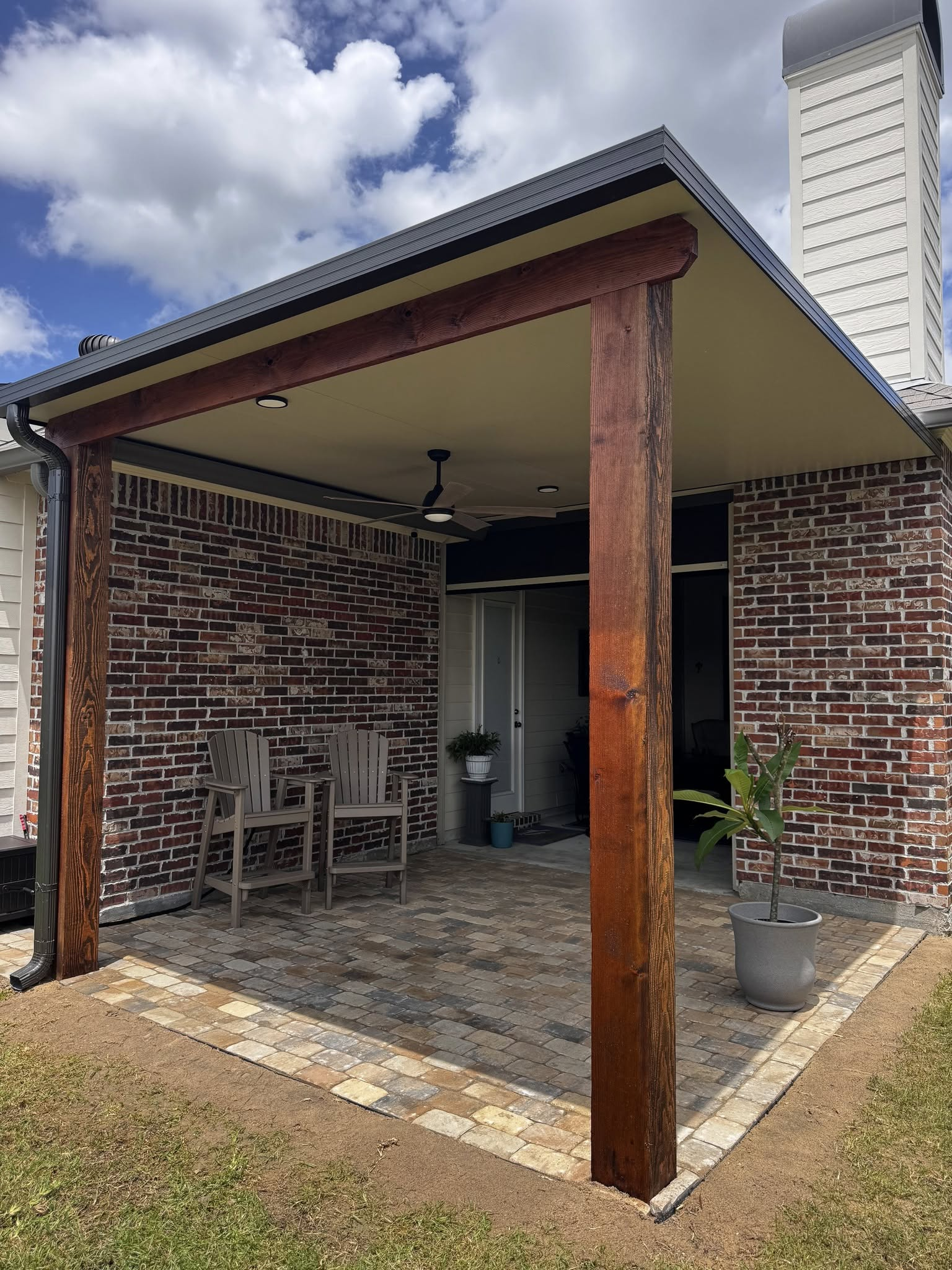 Patio with brick walls and a wooden pergola, furnished with chairs, facing a door.