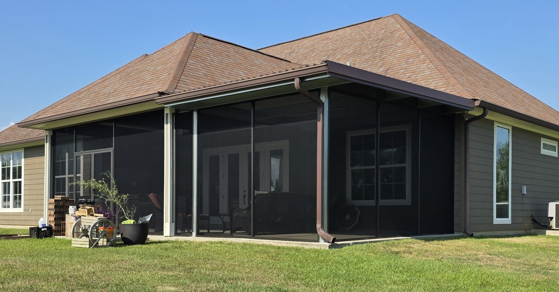 Screened-in porch on a house with dark screens, brown roof, and green grass.
