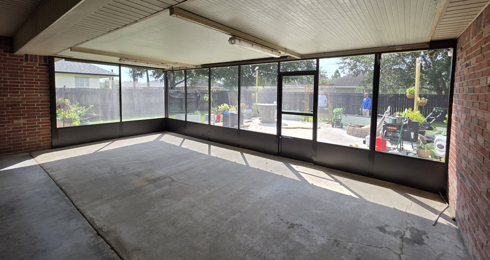 Enclosed patio with concrete floor, screened walls, door to garden, and brick wall.