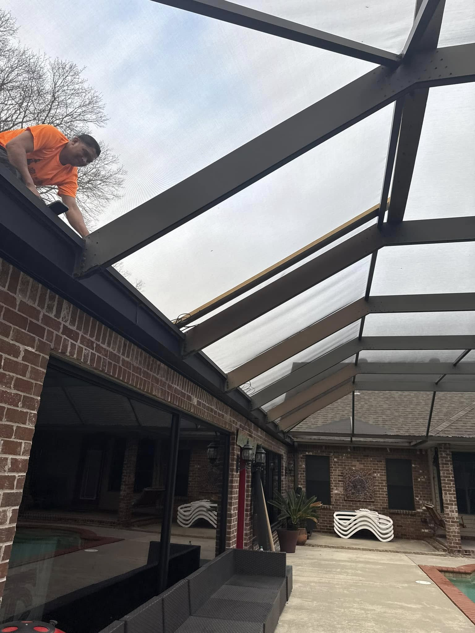 Man in orange shirt working on a screen enclosure roof attached to a brick building.