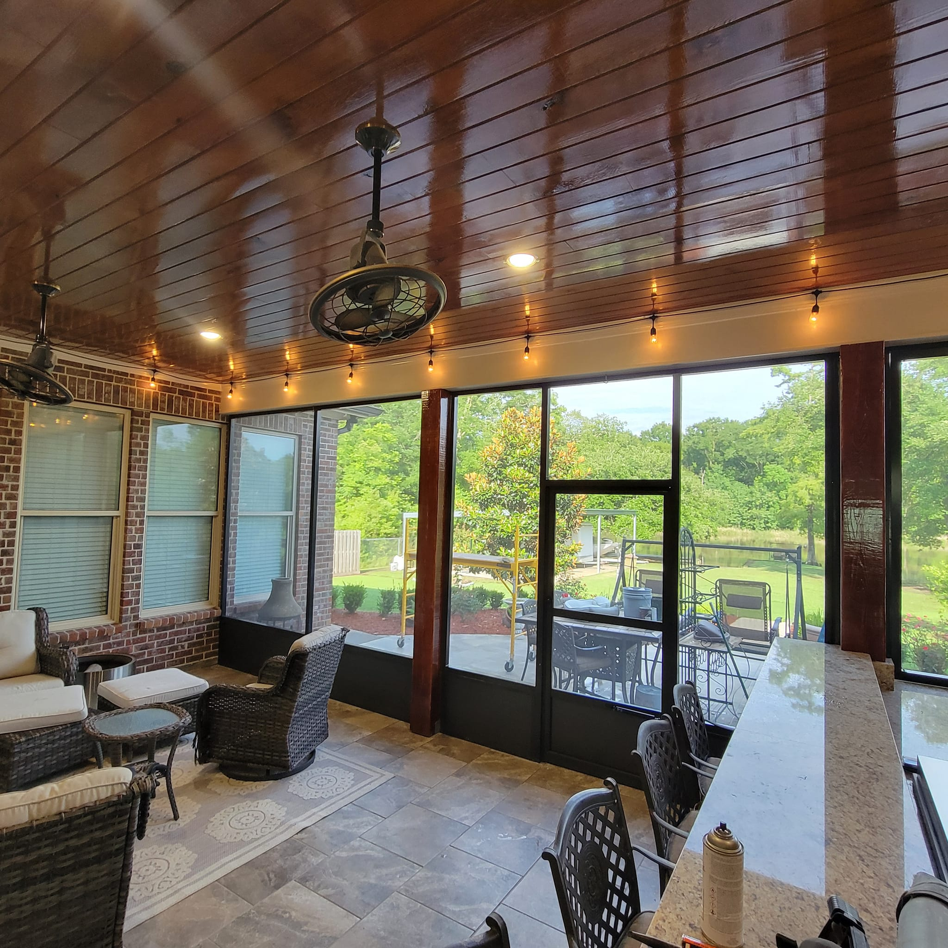 Screened-in porch with seating, bar, ceiling fans, brick columns, and a view of a green yard.
